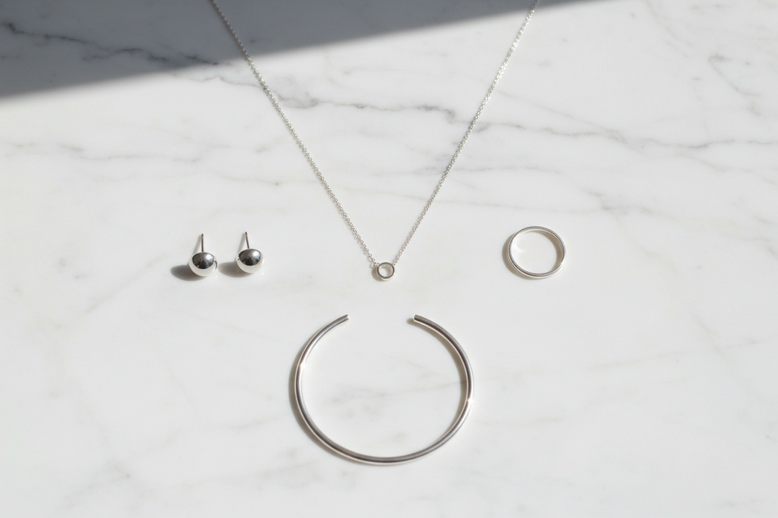 Gioielli minimalisti in argento 925 su marmo bianco: collana sottile, orecchini a lobo, anello fascia e bangle - Gabriel Milano